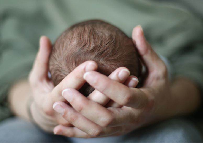 Gros plan sur 2 mains adultes qui soutiennent la tête d’un nouveau-né