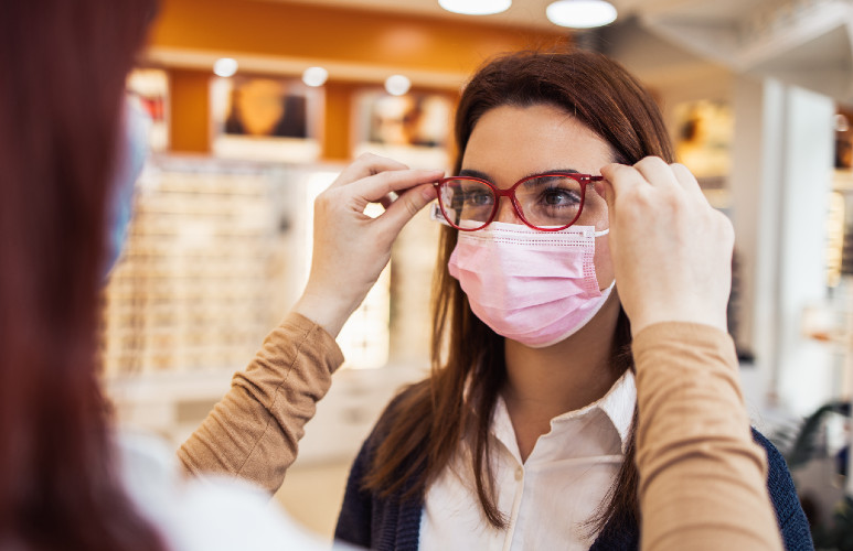 Une femme masquée essaye une paire de lunettes chez un opticien