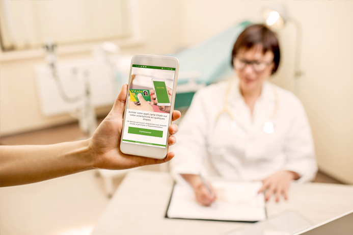 Personne chez le médecin présentant un smartphone avec l'appli carte vitale affichée à l'écran