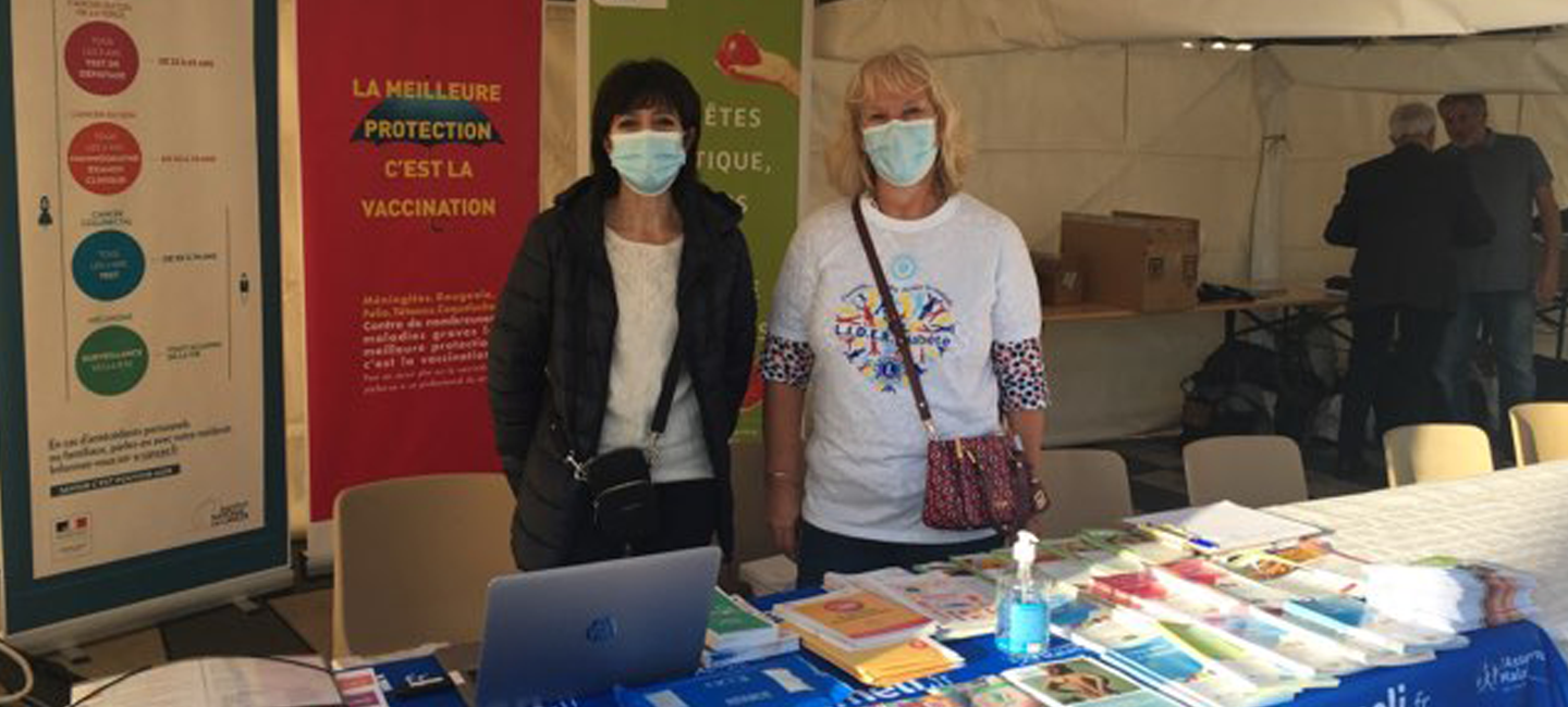  Deux femmes qui tiennent un stand prévention santé avec des brochures étalées sur une table 