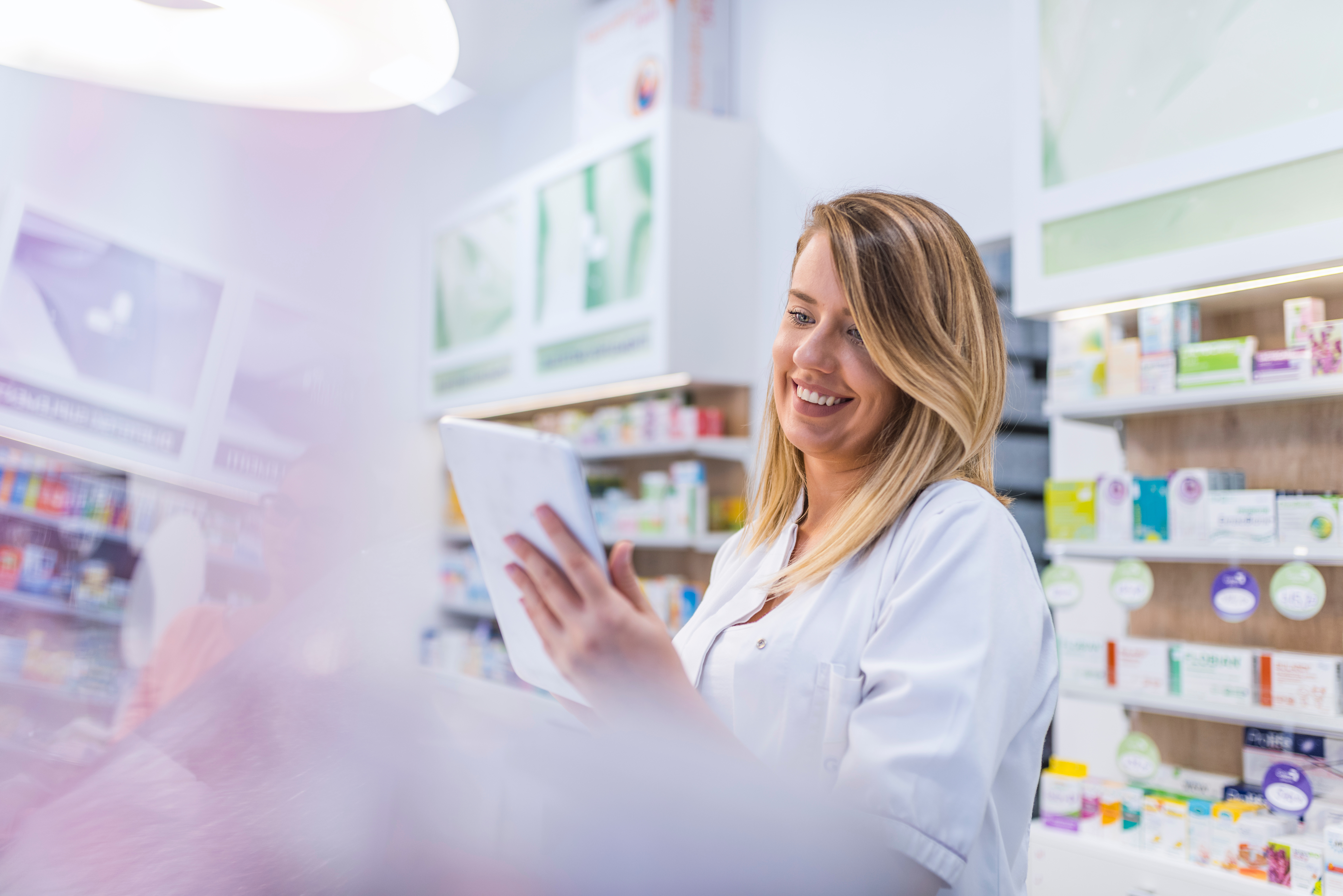 Pharmacienne qui regarde une tablette debout derrière le comptoir d'une pharmacie