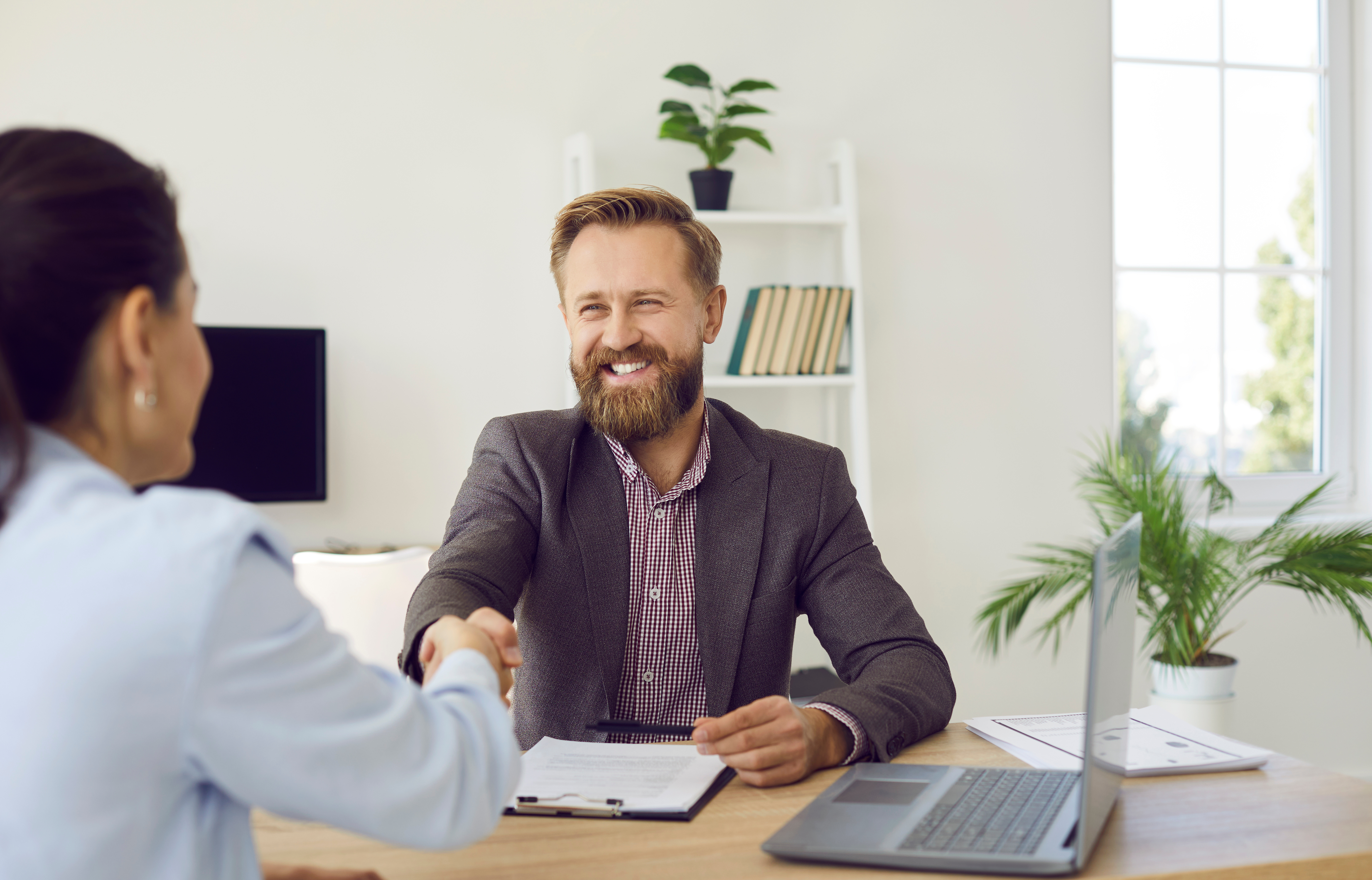 homme assis derrière un bureau échangeant une poignée de mains avec une femme assise de l'autre côté du bureau