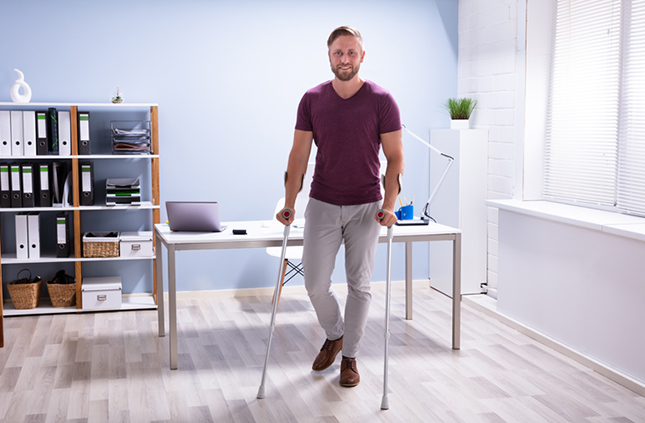 Homme à la maison debout avec des béquilles devant un bureau