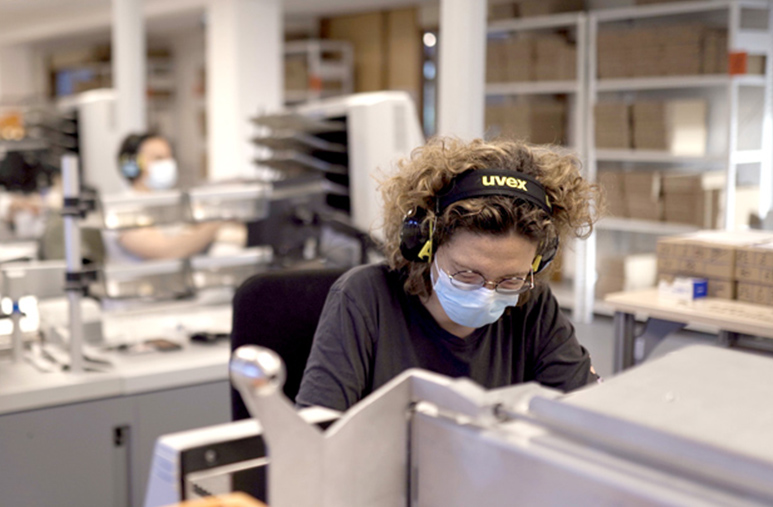 Femme assise à un bureau qui porte un masque et un casque sur les oreilles en situation de travail sur la plateforme flux entrants