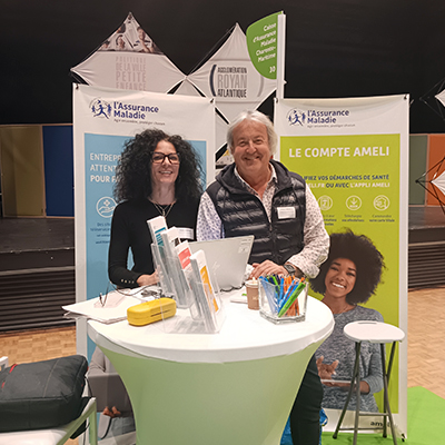 Stand d’information avec deux représentants de la CPAM derrière un mange-debout.