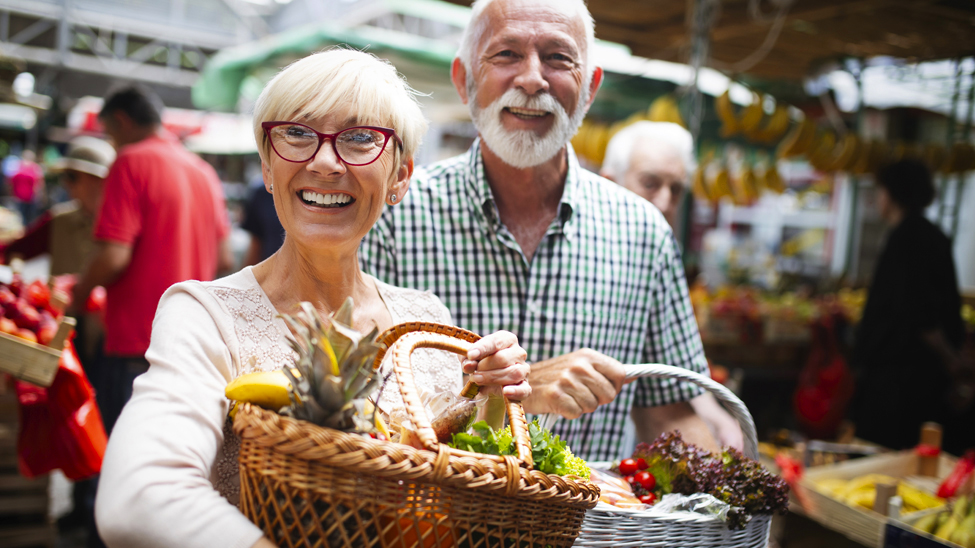 Un couple de seniors au marché avec chacun un panier de fruits et légumes