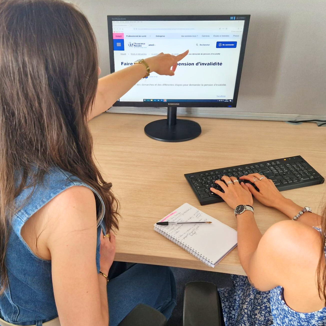 photo de deux personnes de dos, l'une qui montre quelque chose à l'autre sur un écran d'ordinateur