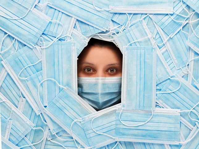 Femme masquée avec un masque chirurgicale qui regarde tout droit à travers un mur de masques chirurgicaux