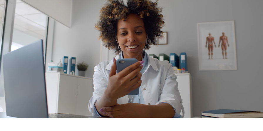 Photo illustrant l'article. Elle représente une médecin souriant à son bureau, avec un smartphone en main.