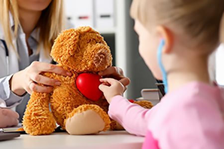 photo représentant une jeune fille touchant le coeur d'un ours en peluche, face à un médecin.