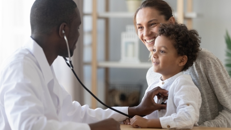 Un médecin traitant écoute le coeur d'un enfant qui est assis sur les genoux de sa mère, avec un stétoscope